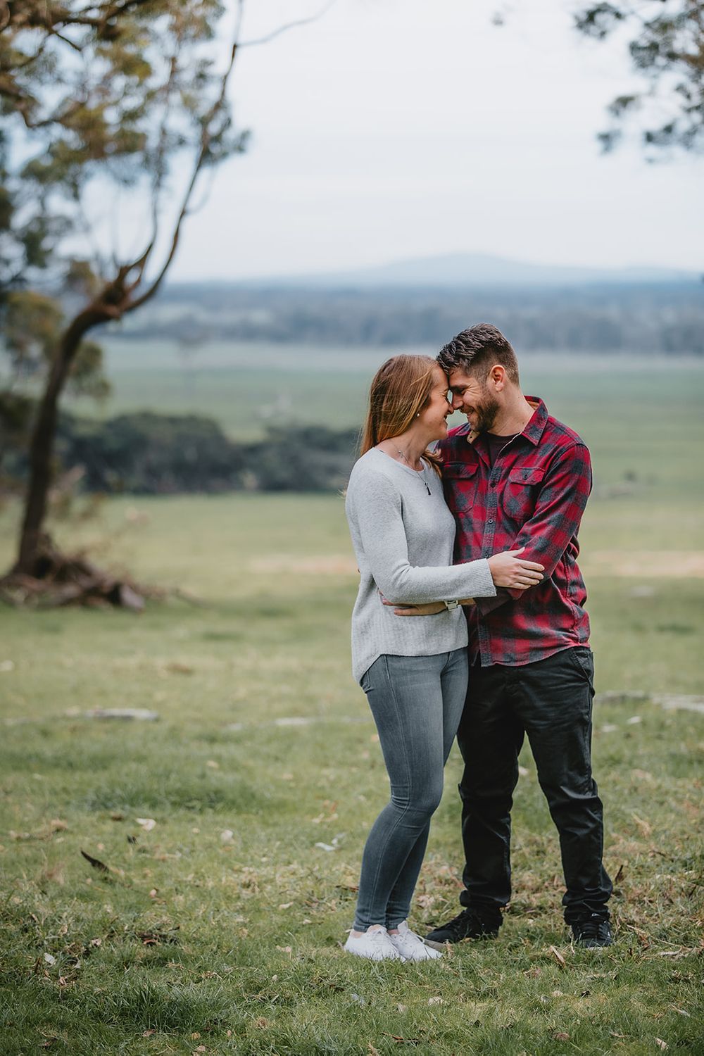 A couple shares an intimate moment together on a grassy hillside overlooking a scenic landscape.