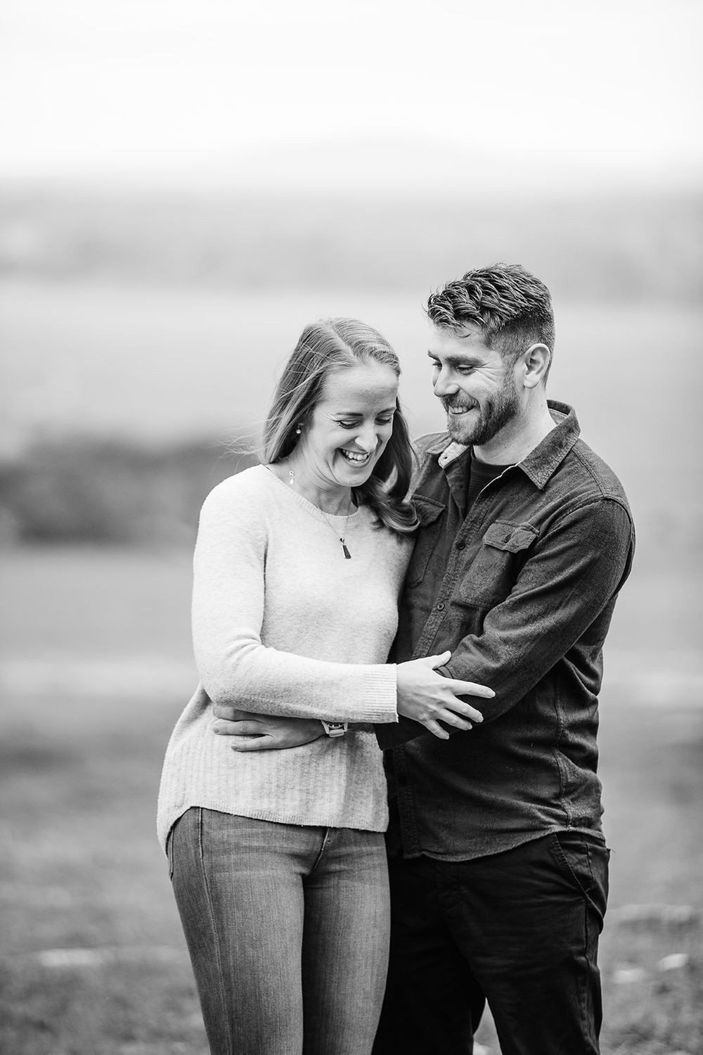 Black and white portrait of couple sharing intimate moment in open field.