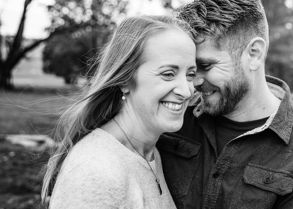 Candid black and white photo of couple laughing together in nature.