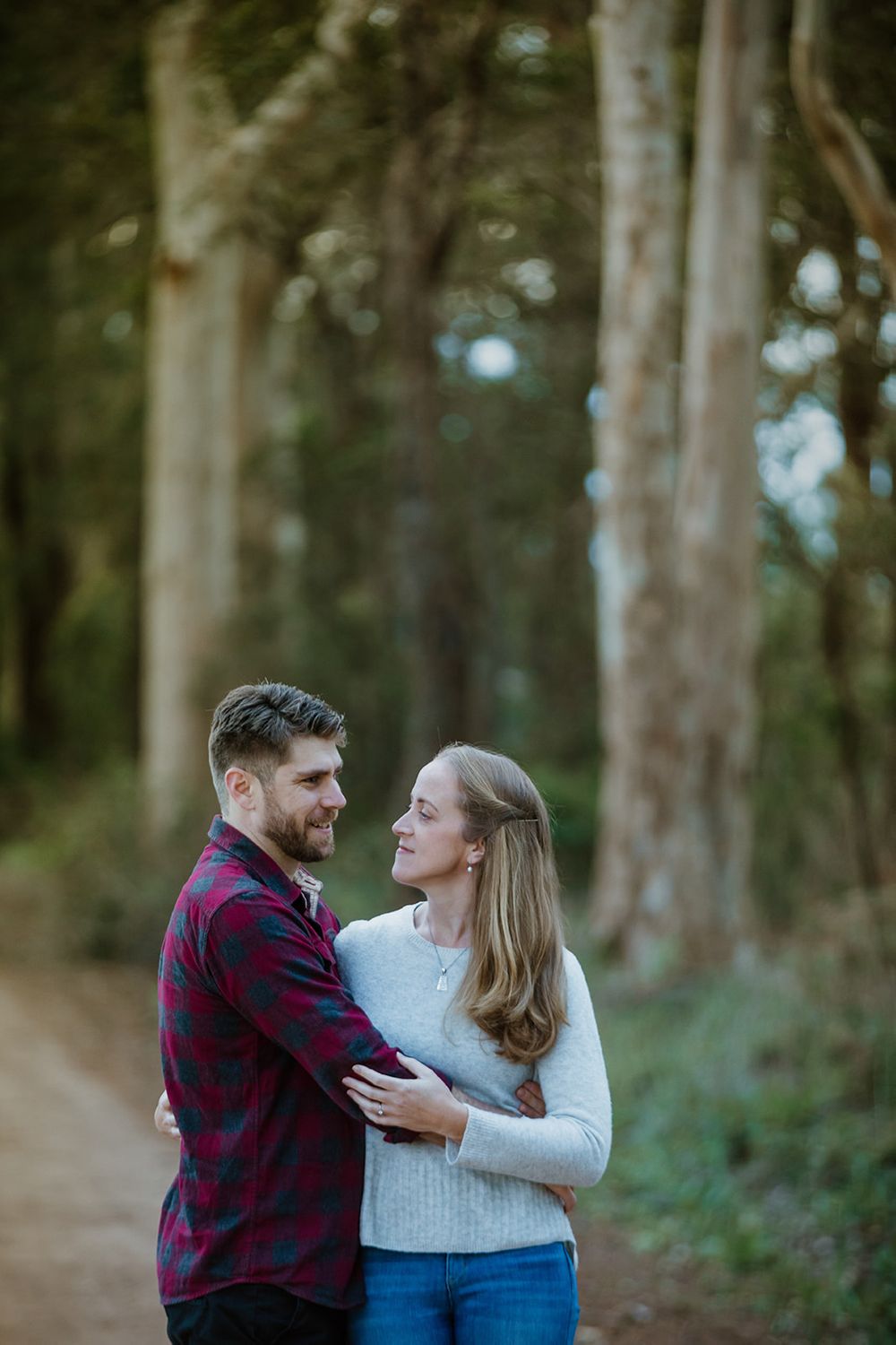 Couple embracing among tall eucalyptus trees in romantic outdoor setting.
