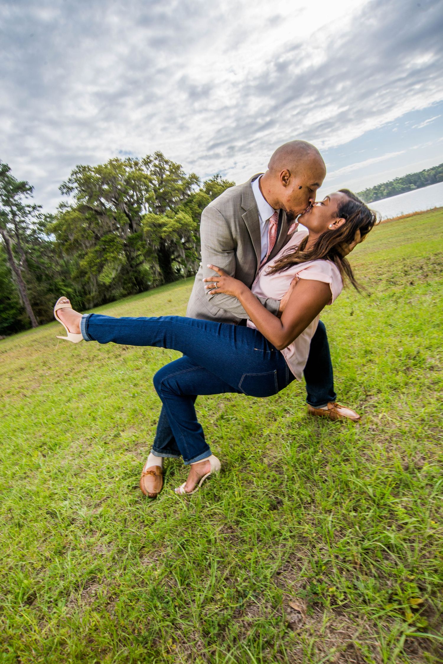 Romantic outdoor photo of a couple performing a dramatic dip pose on grassy hillside.