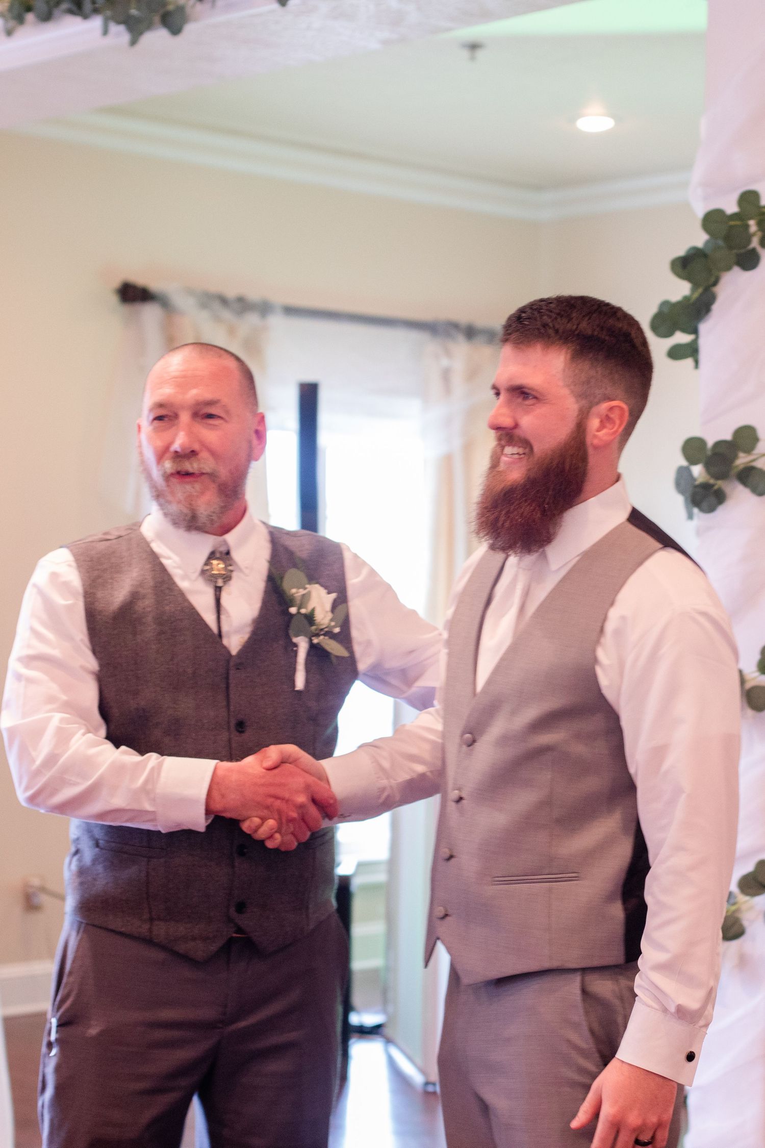 Wedding party members in grey vests and white shirts share congratulatory handshakes.