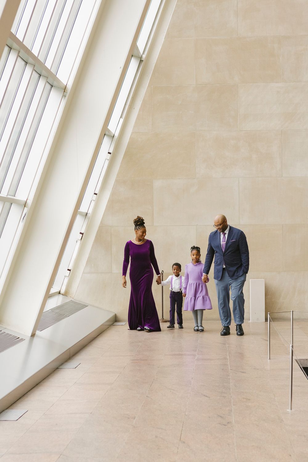 Family of four, holding hands and walking in awe-inspiring harmony inside the Temple of Dendur at The Met
