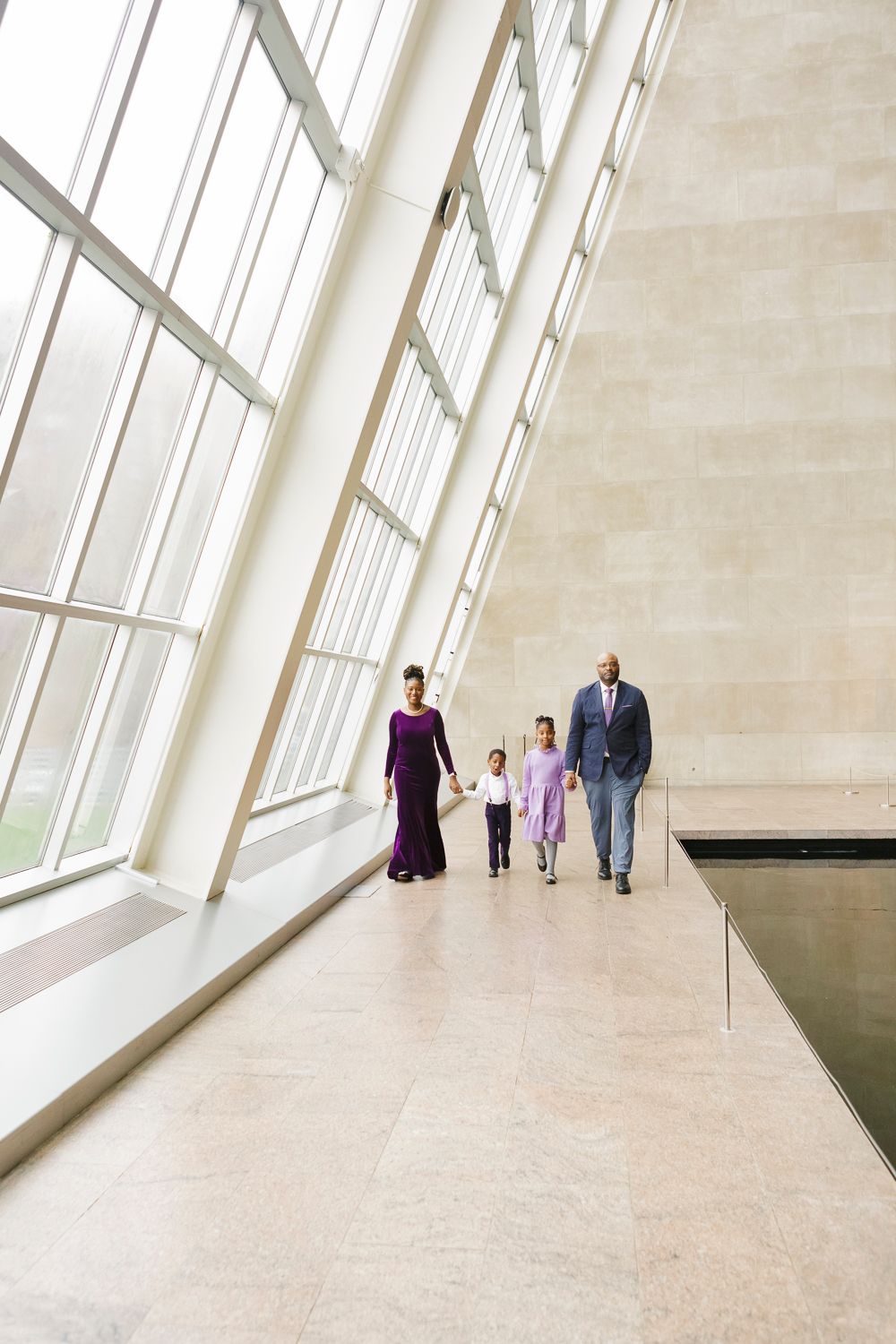 Family of four, holding hands and walking inside the Temple of Dendur captured by NYC photographer Paula Ortiz
