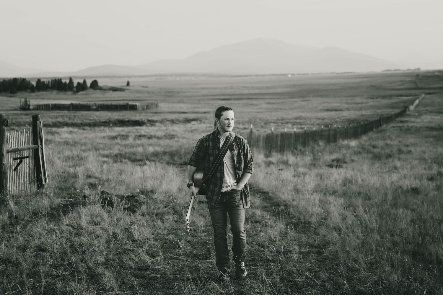 Black and white landscape photograph of vast open plains with mountains and senior boy in the distance.
