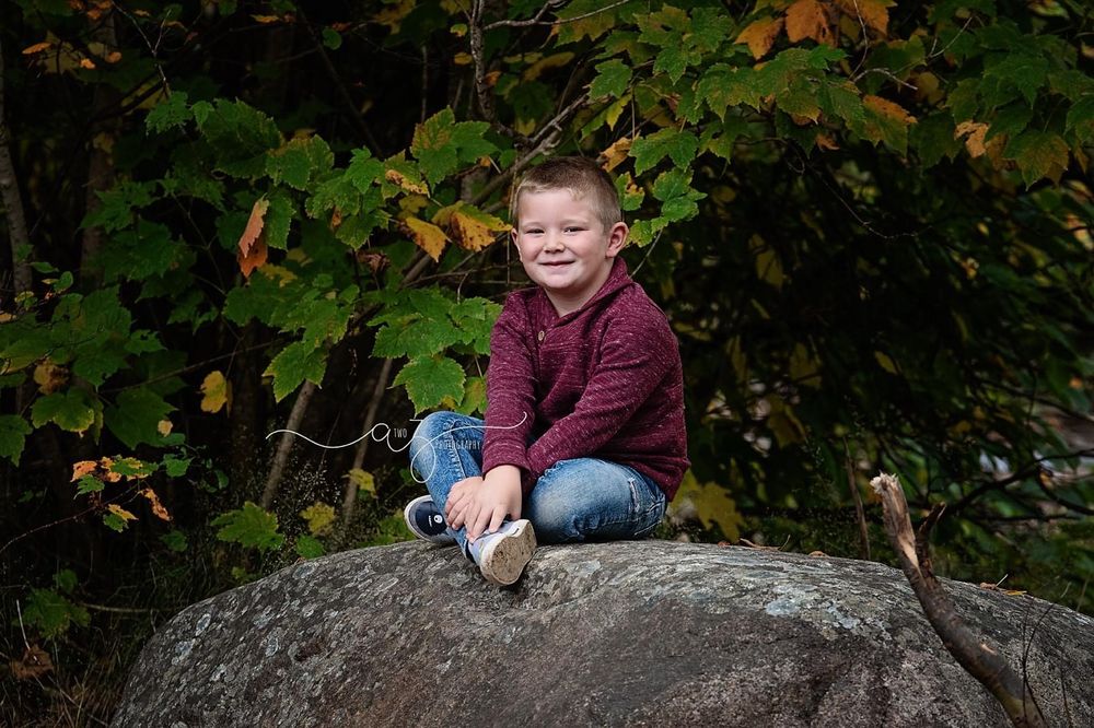 Young child sitting on large boulder surrounded by fall foliage.