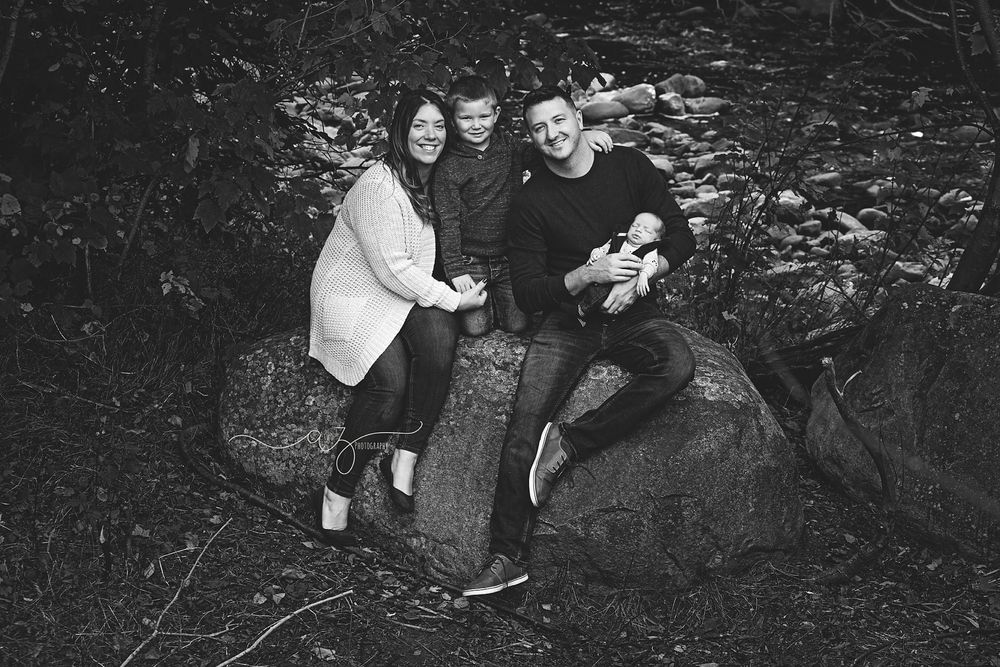 Candid black and white photo of a family group sitting together on a large rock outdoors.