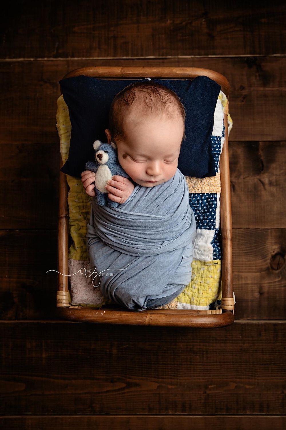 Sleeping newborn wrapped in gray swaddle with toy laying in wooden crate.