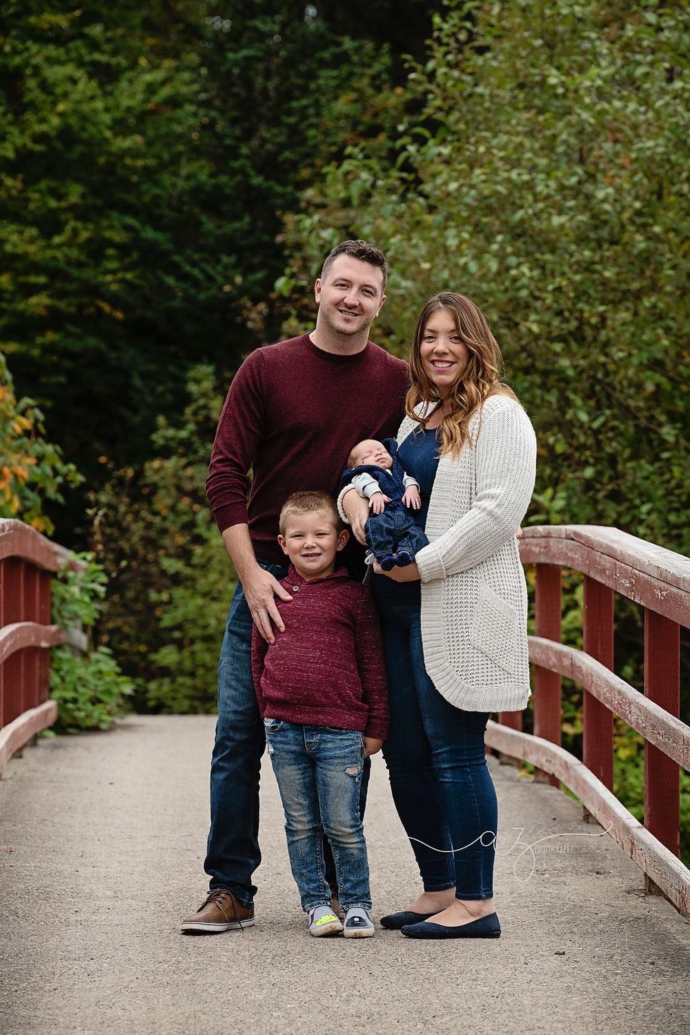 Family of four standing together on red bridge during fall photo session.
