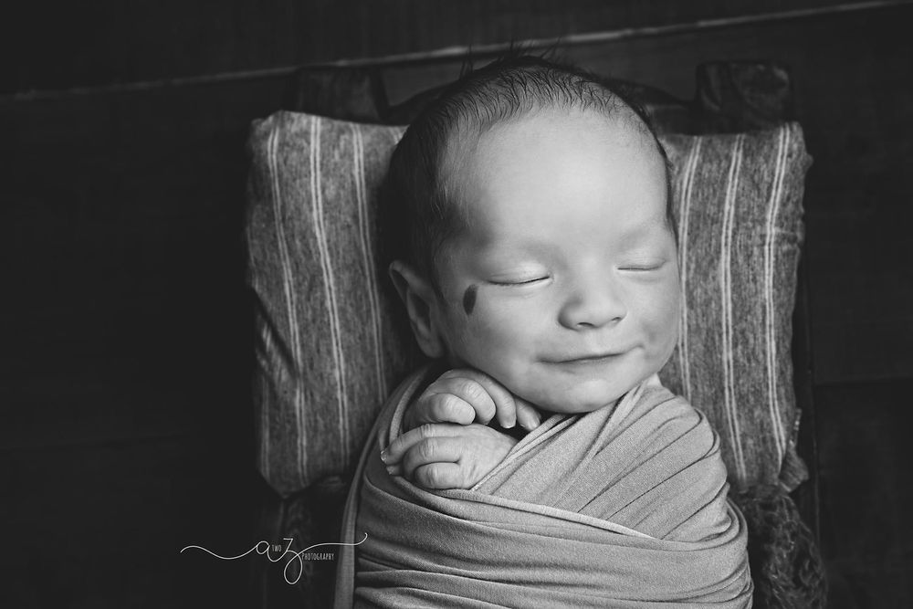 Black and white portrait of sleeping newborn wrapped in soft fabric.