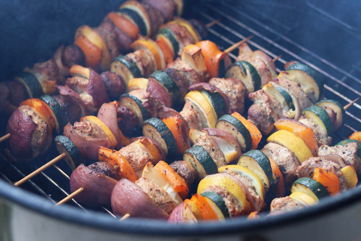 Multiple skewers of grilled meat and vegetables cooking on barbecue grill.
