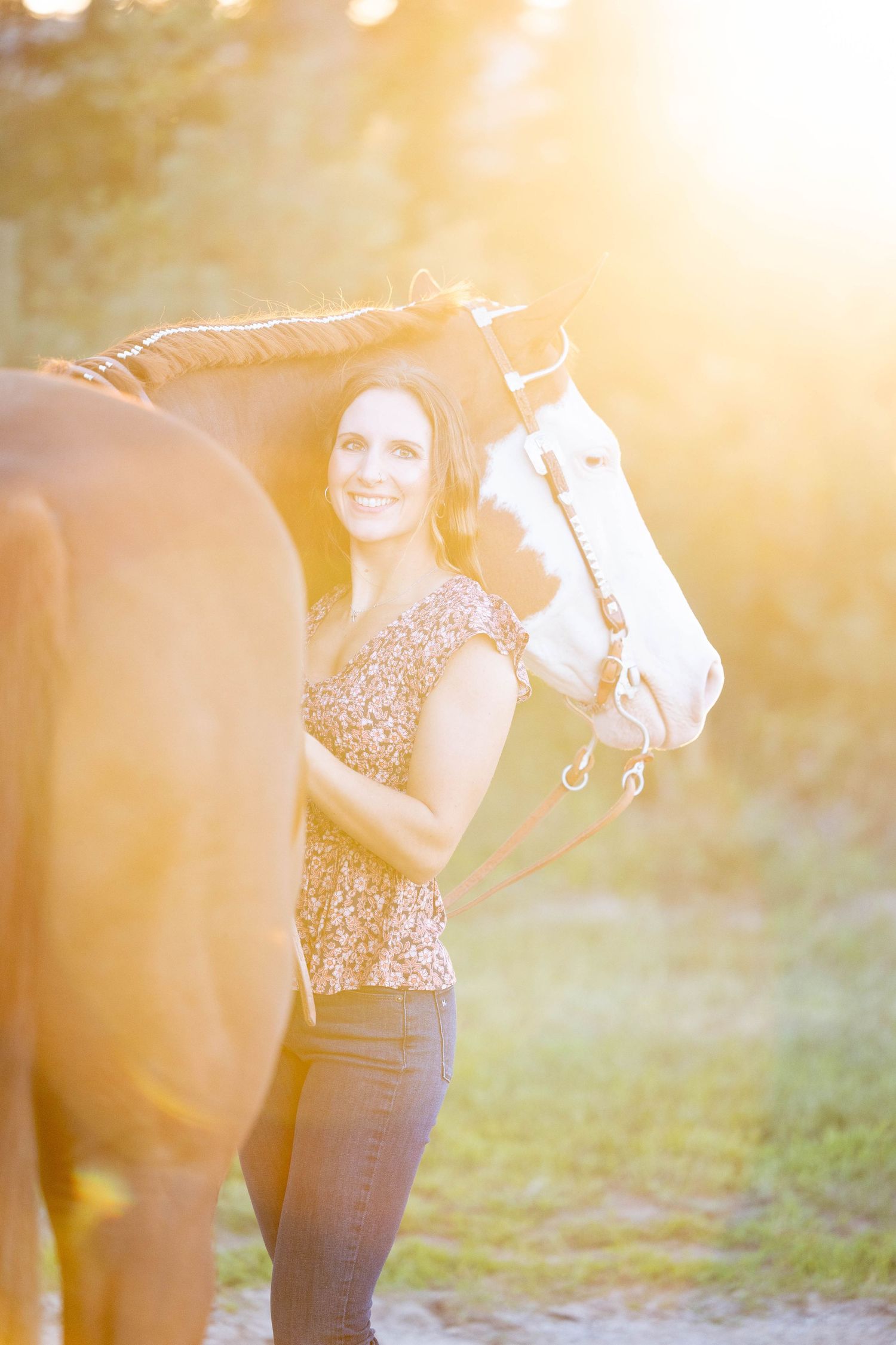 Girl in golden hour wearing a flowered shirt with her chestnut gelding peeking over her shoulder