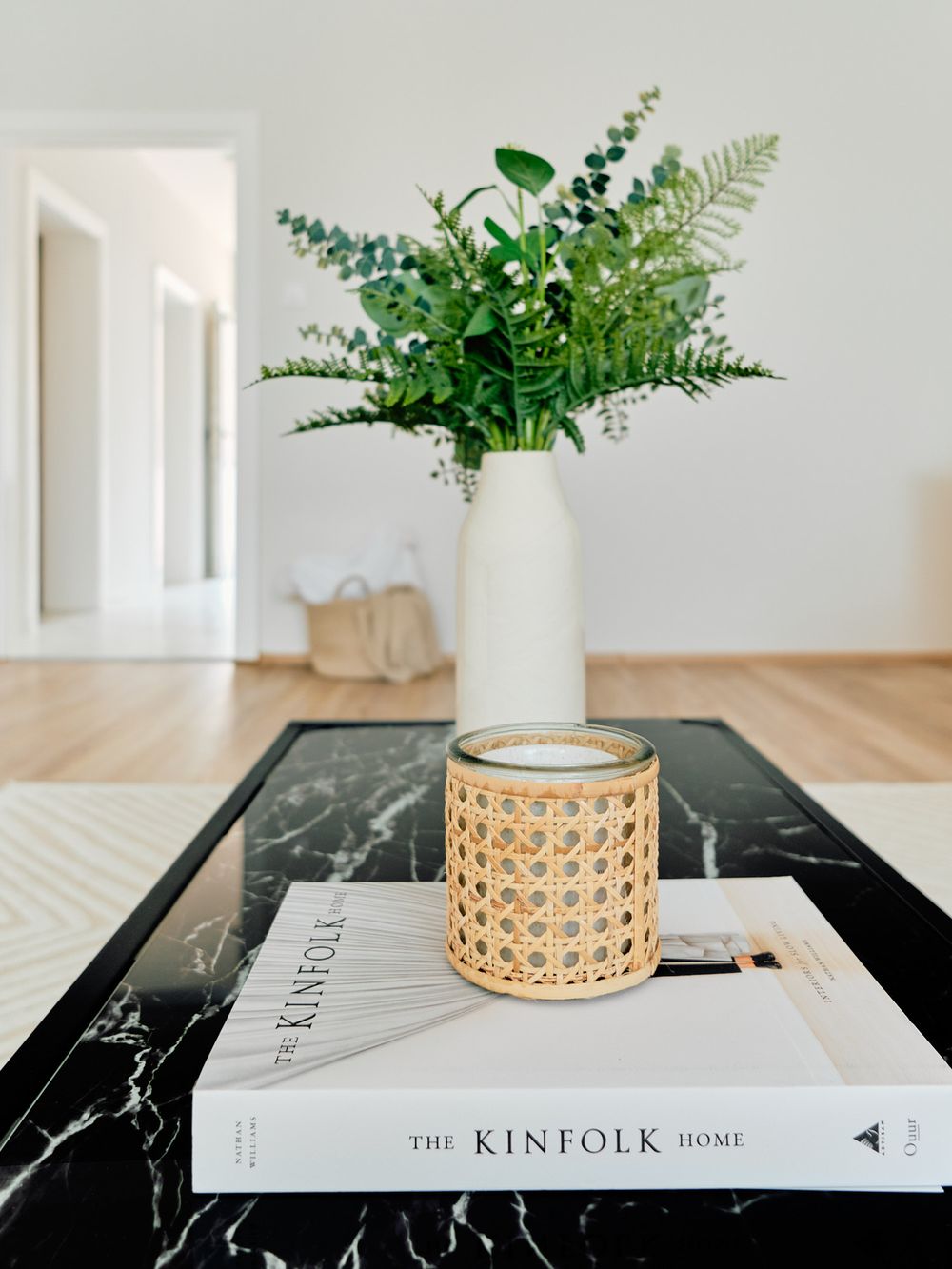 White vase with ferns on marble coffee table with Kinfolk book and rattan candle holder.