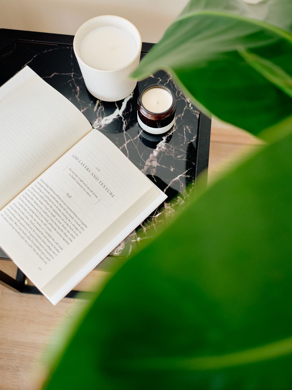 Open book and drinks on marble surface with green plant leaf in foreground.