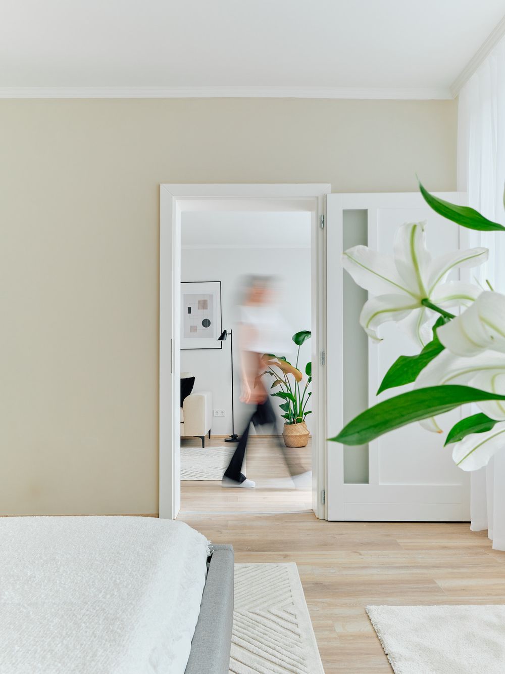 White modern bedroom doorway with lily plant and mirror reflection.
