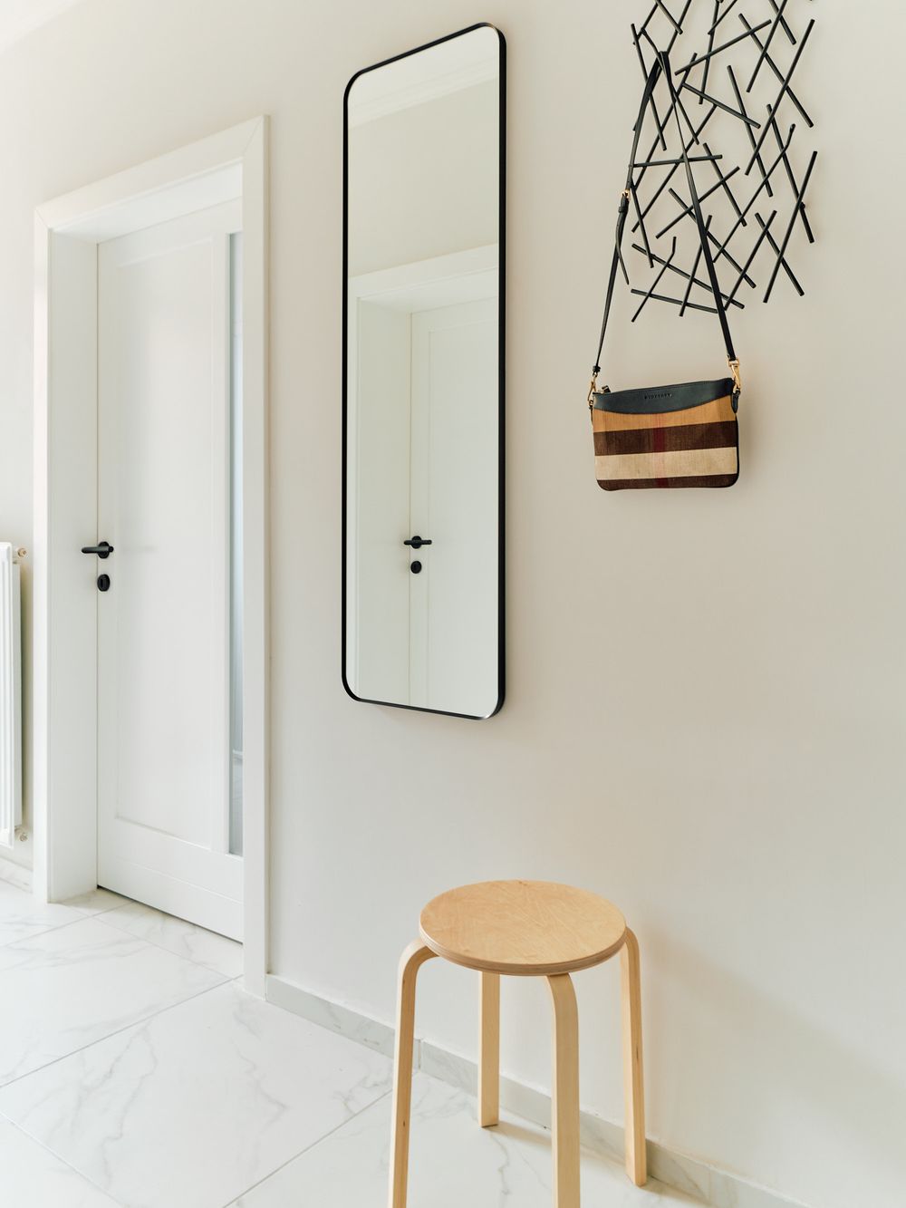 Modern entryway with full-length mirror, wooden stool, and decorative wall art.
