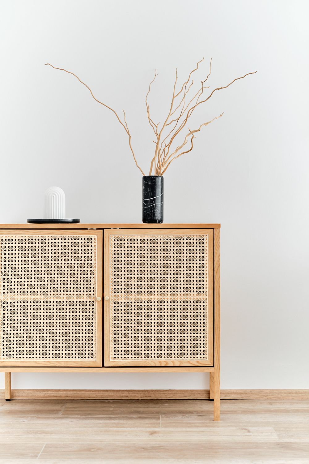 Minimalist rattan sideboard with dried branches in a black vase against white wall.