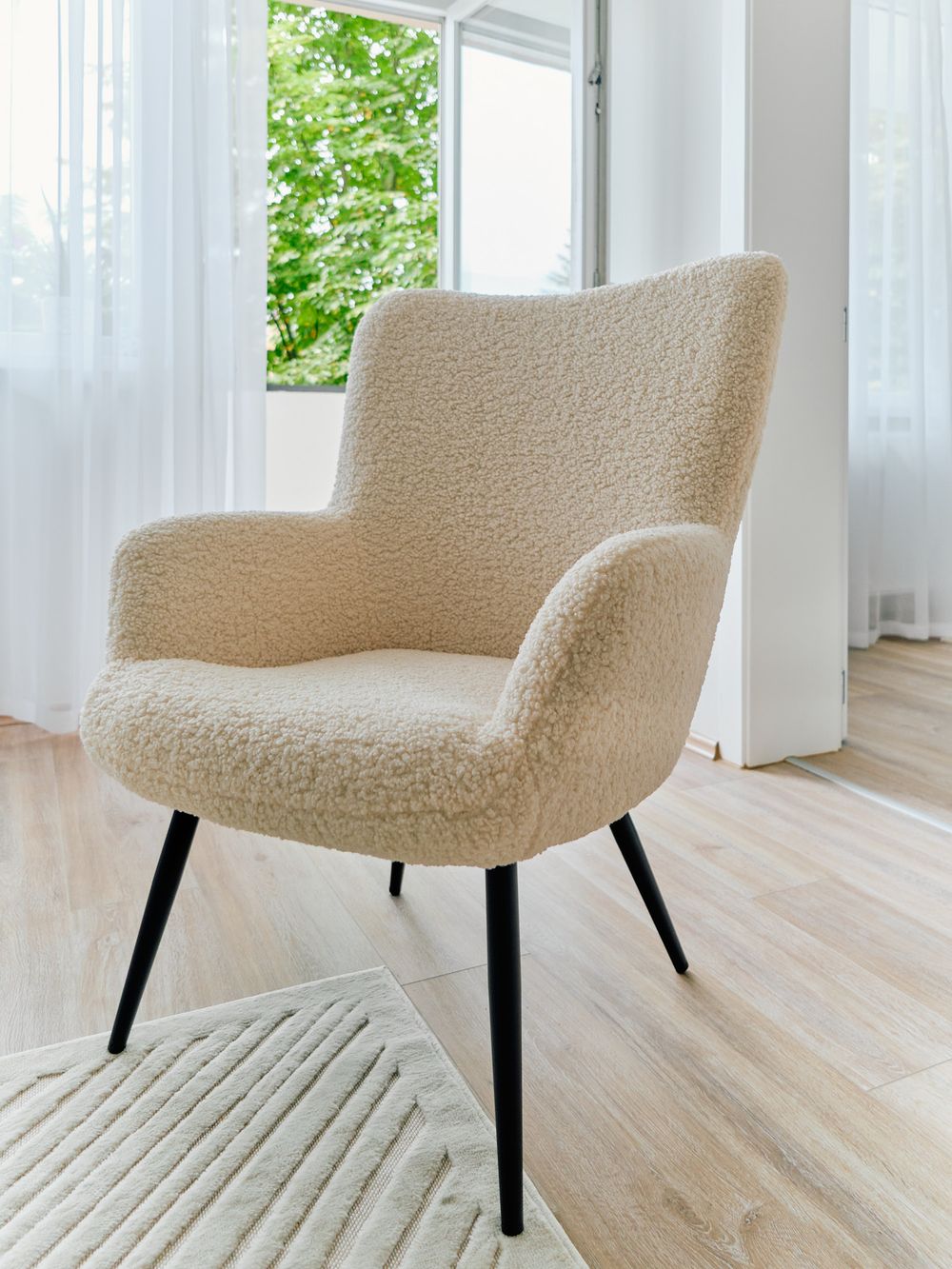 Cozy cream-colored teddy fabric armchair with black legs near a bright window.