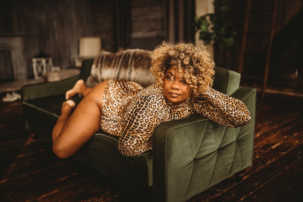 Woman in leopard print outfit posing on a green velvet chair in a moody studio setting.