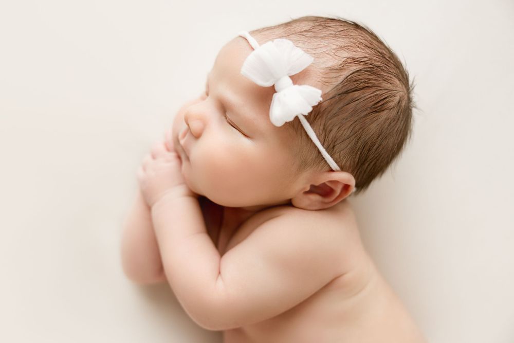 Sweet and simple newborn photograph. Newborn baby girl with a white bow.