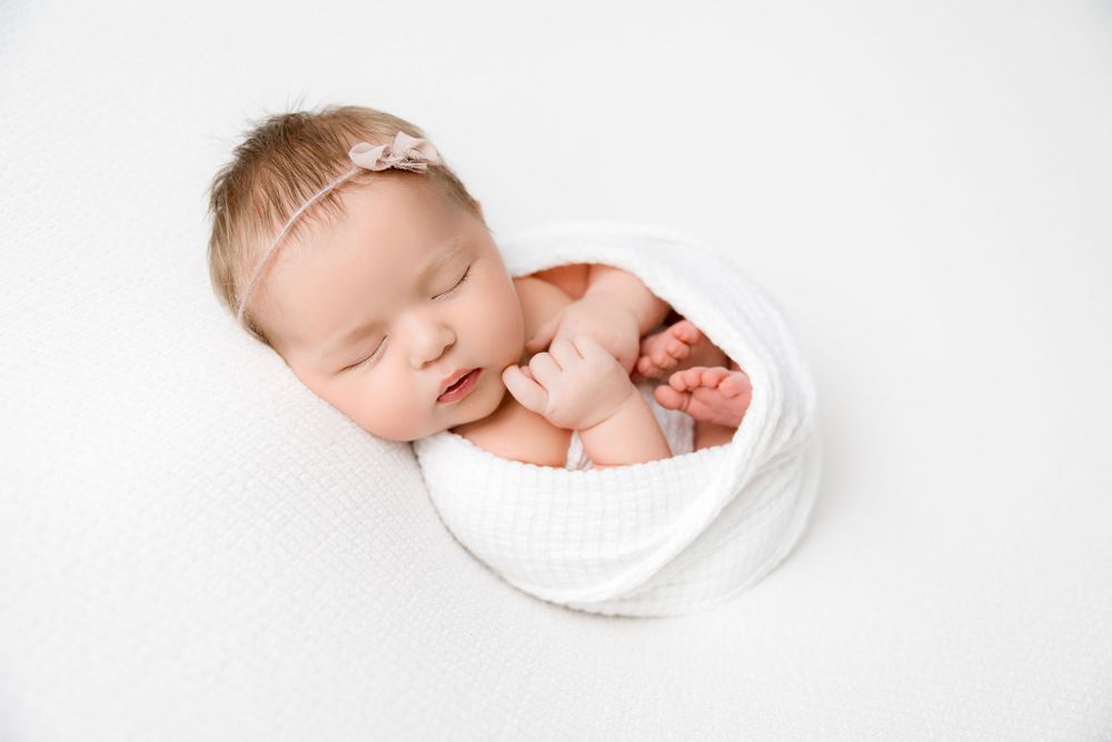Newborn baby girl in on a white background with a half wrap, with hands and feet out, wrapped in white