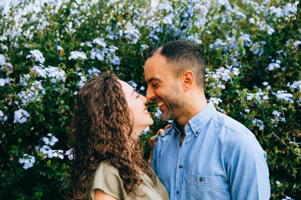 A romantic couple shares an intimate moment in front of blooming white daisies on a sunny day.