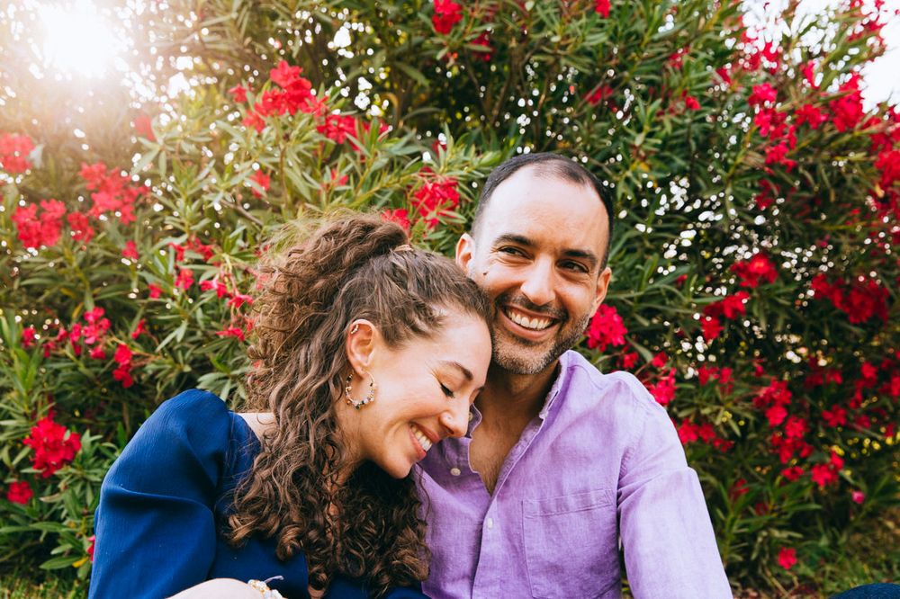 A tender moment shared against vibrant red flowering bushes in golden sunlight.