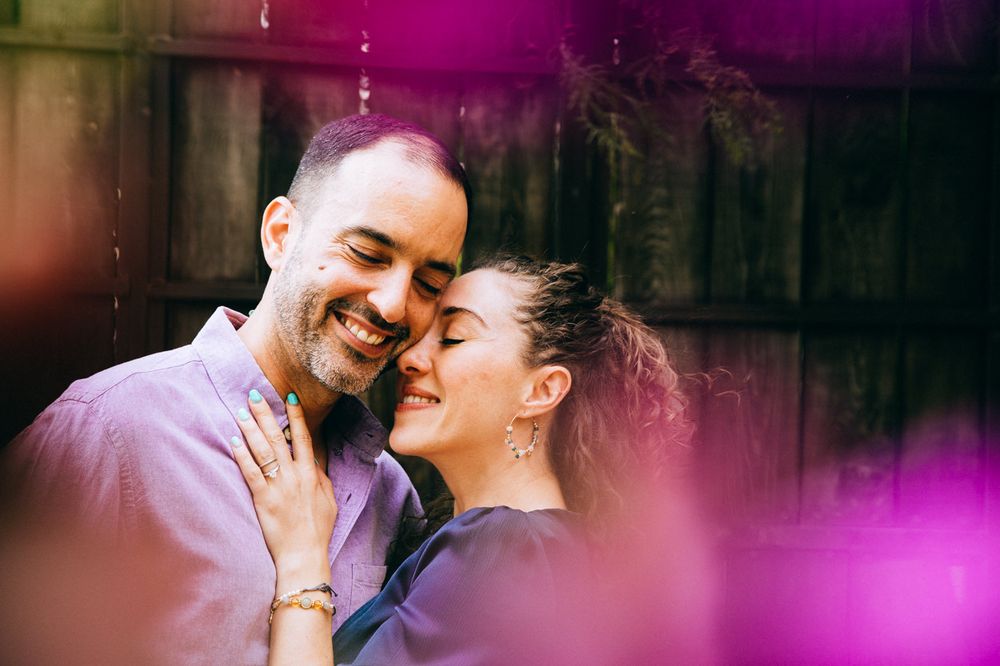 An intimate moment captured with purple light flares and wooden fence backdrop.