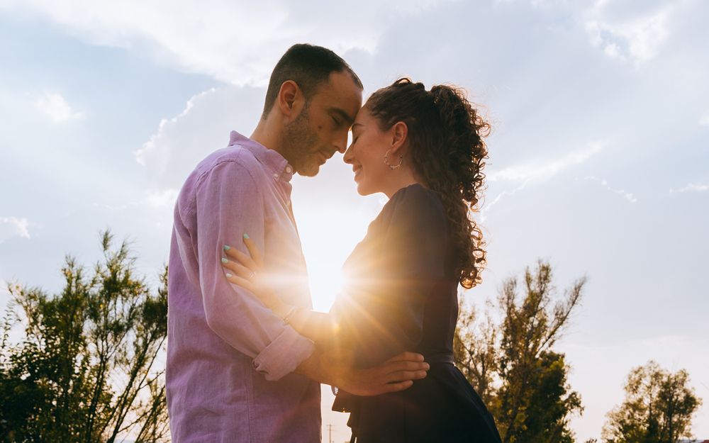 Couple shares a romantic kiss while embracing at sunset with sunlight streaming between them.