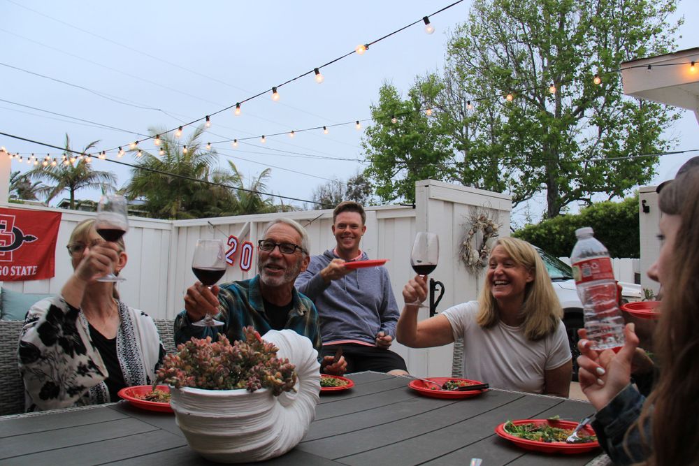 Outdoor dinner party with string lights and people gathered around a table.