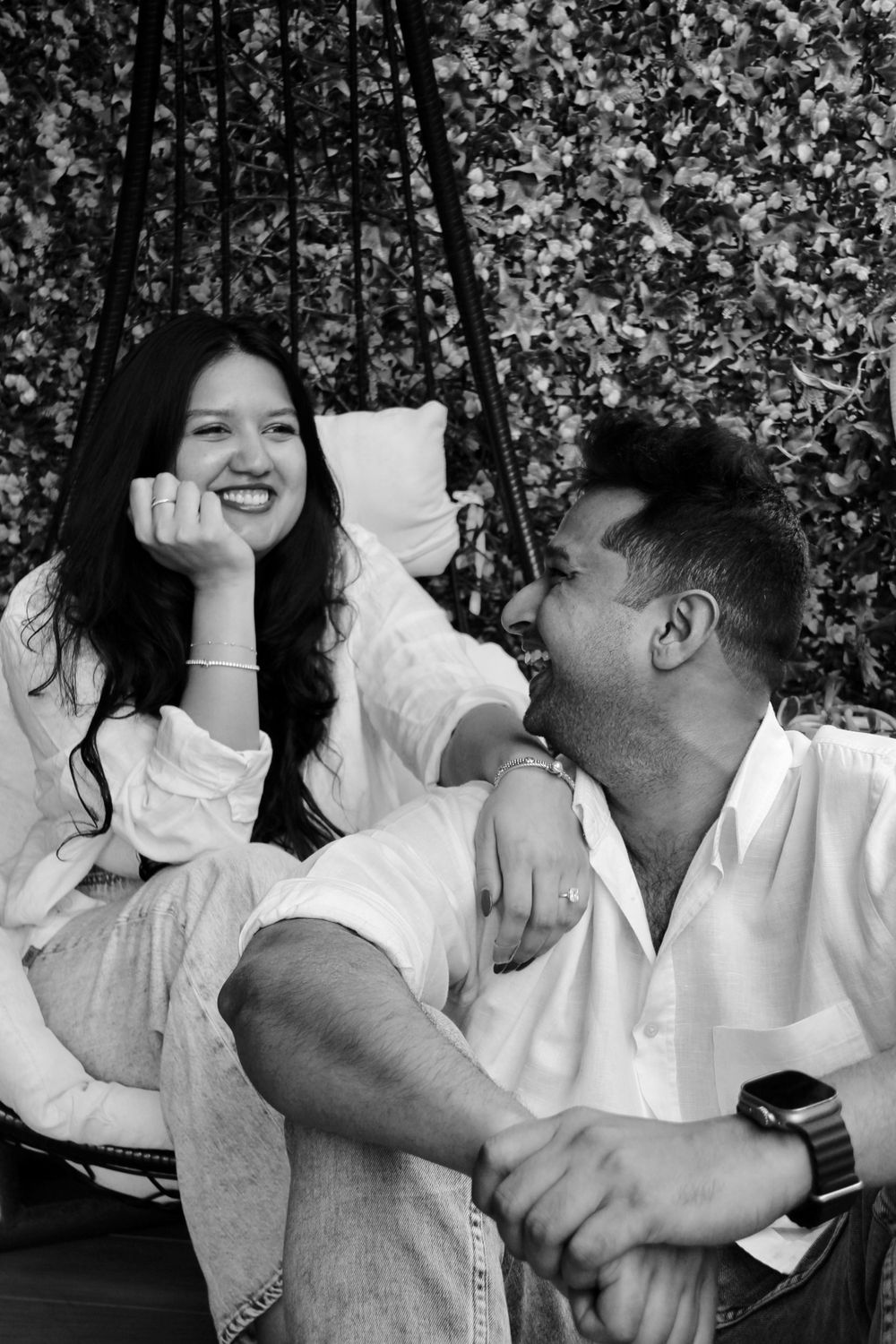 Candid black and white photo of a couple laughing together on a porch swing.