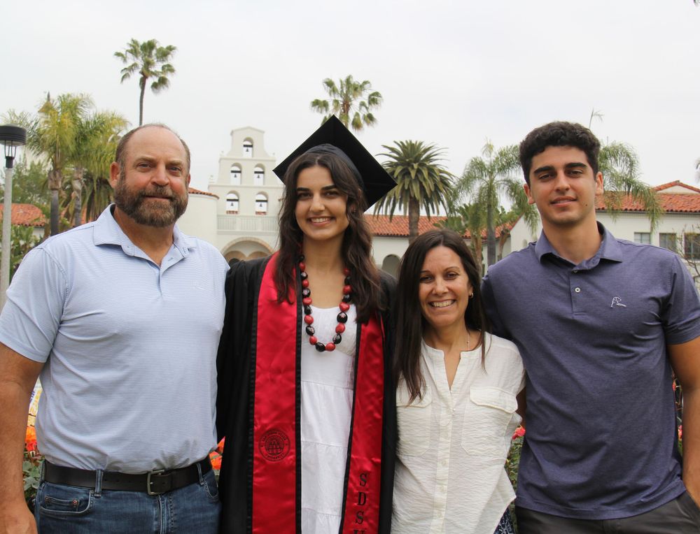 Family graduation photo taken in front of a Spanish mission-style building with palm trees.