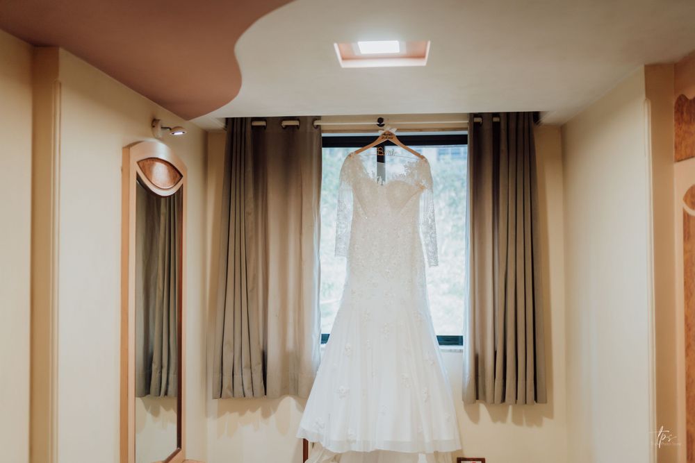 Row of white wedding dresses hanging from wooden hangers in a sunlit dressing room.
