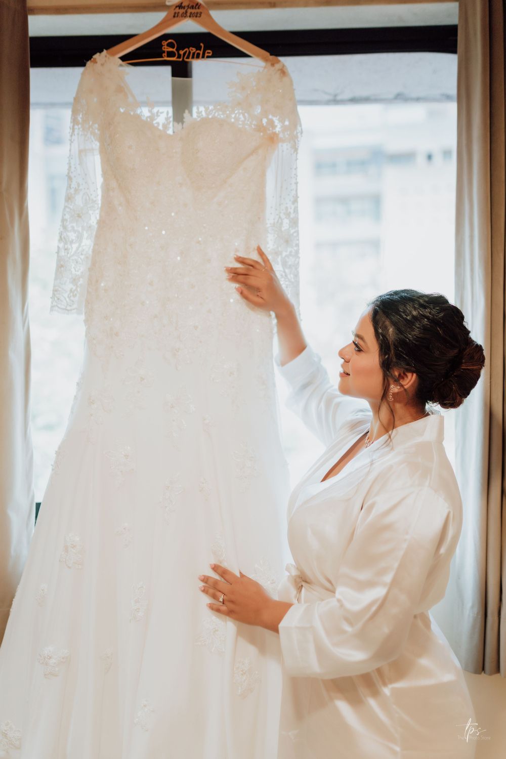 Wedding dresses displayed on hangers while attendants in white robes admire them.