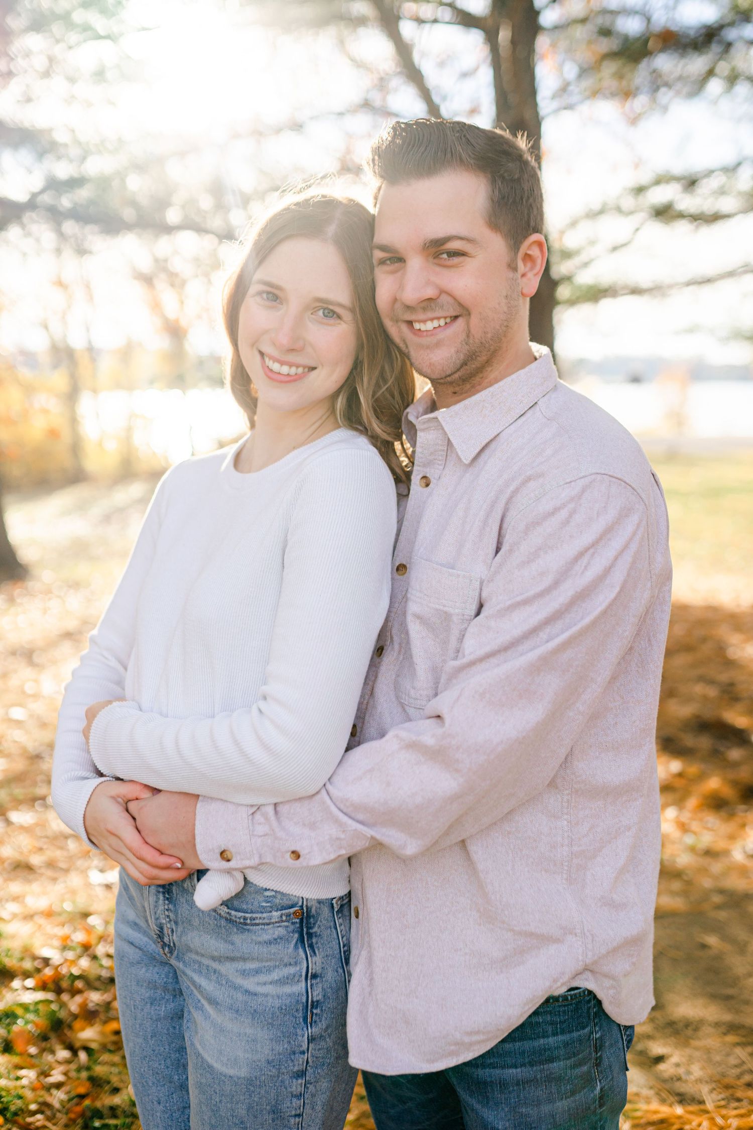 A couple embracing and smiling at the camera in a scenic outdoor setting.