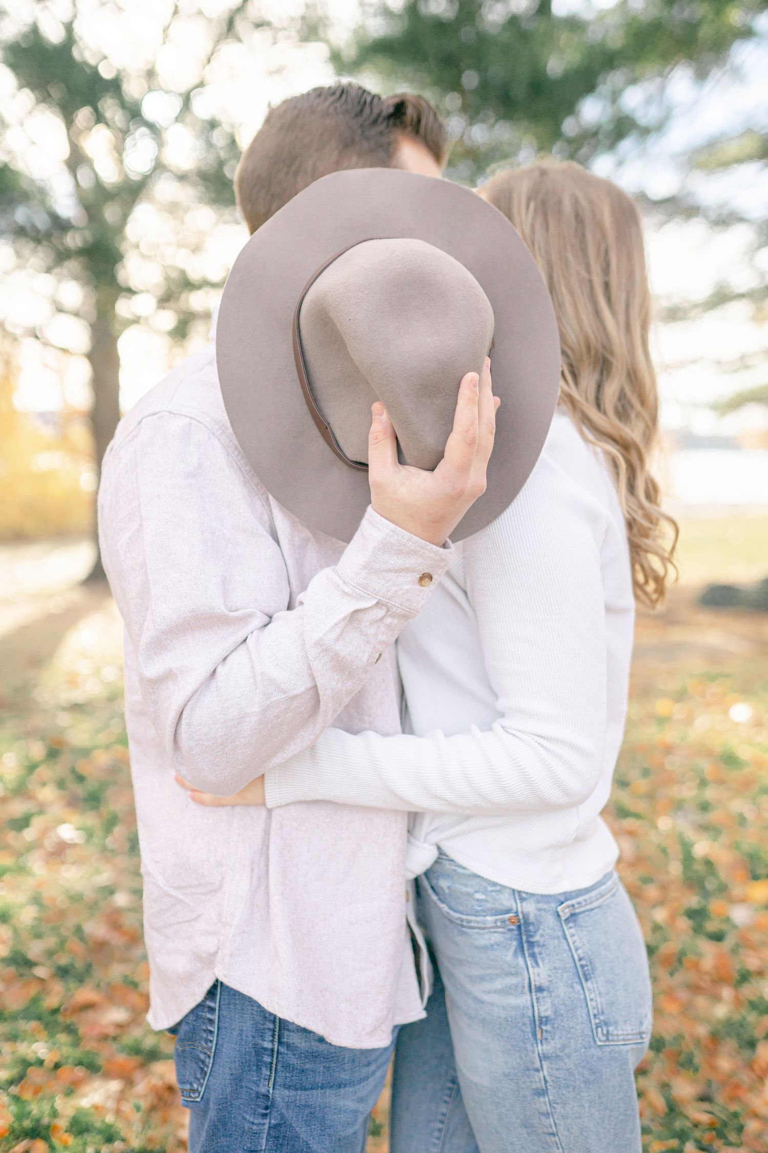 A couple embracing and hiding their faces in a scenic outdoor setting.