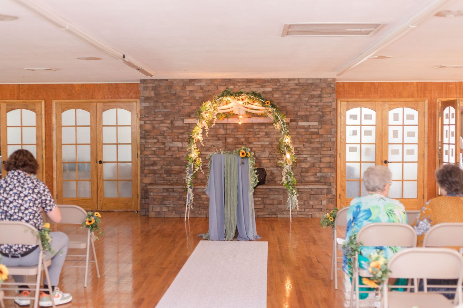 Wedding party and guests gather in an elegant wood-paneled reception hall with brick accent walls and chandeliers.