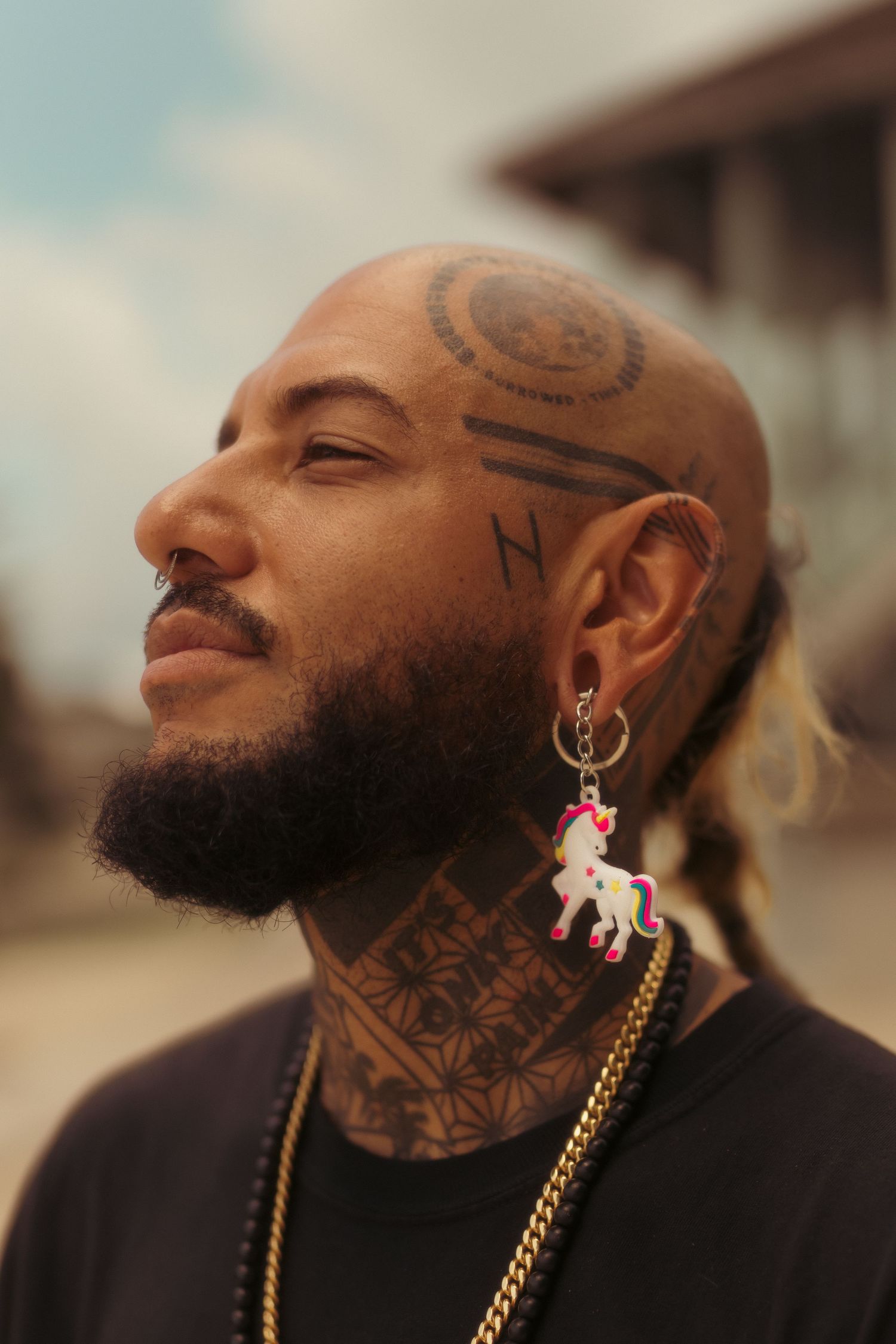 Close-up portrait showing facial tattoos and unicorn earring against blurred background.