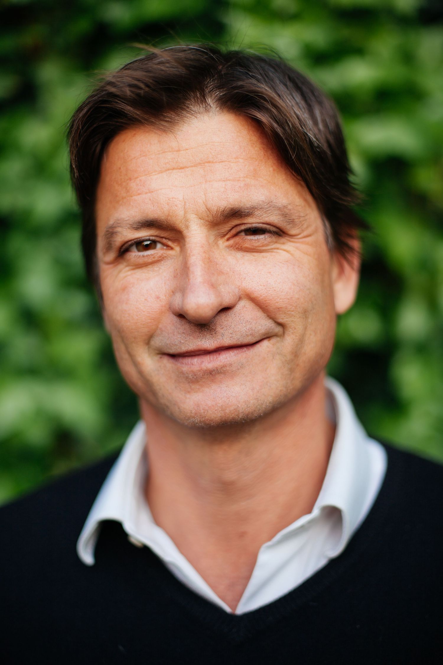 Professional headshot of a person in business casual attire against a green leafy background.