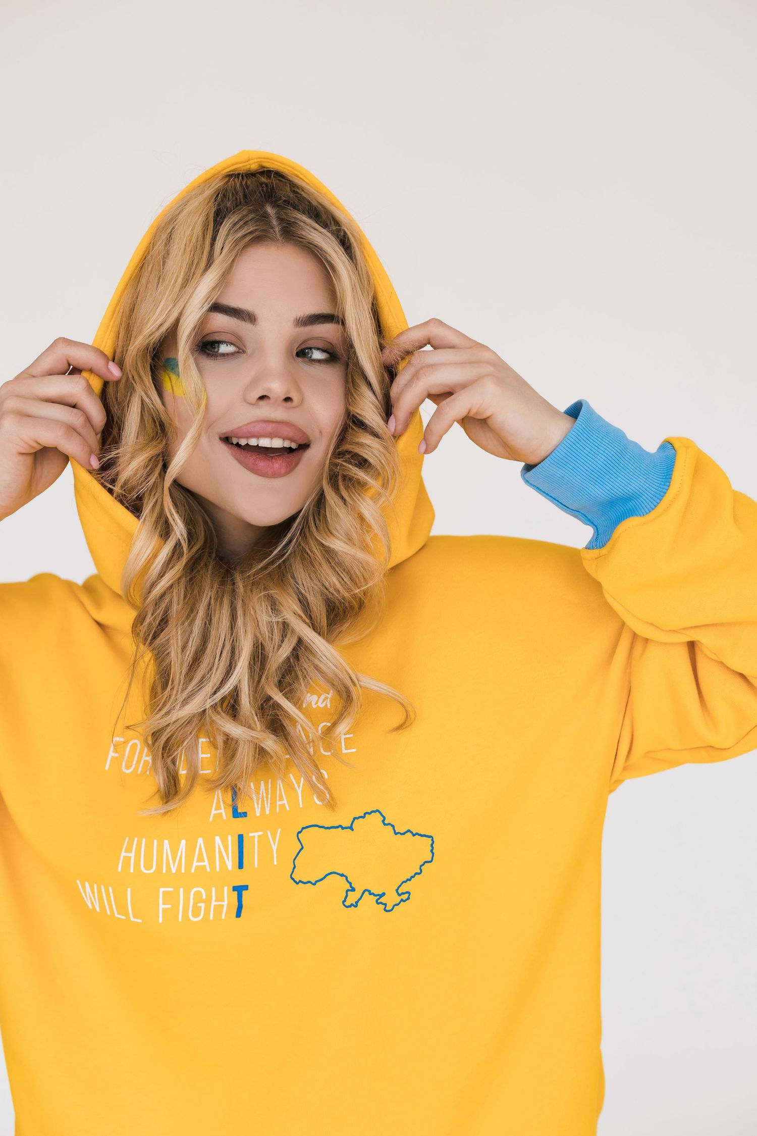Person wearing bright yellow hoodie with graphic design adjusting hood and smiling.