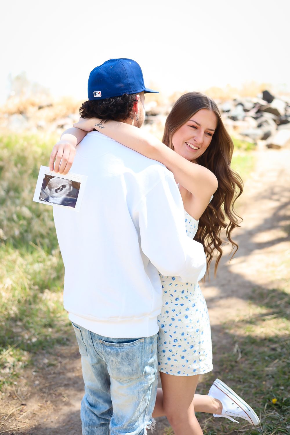 A happy couple sharing a joyful moment while holding an ultrasound photo outdoors.