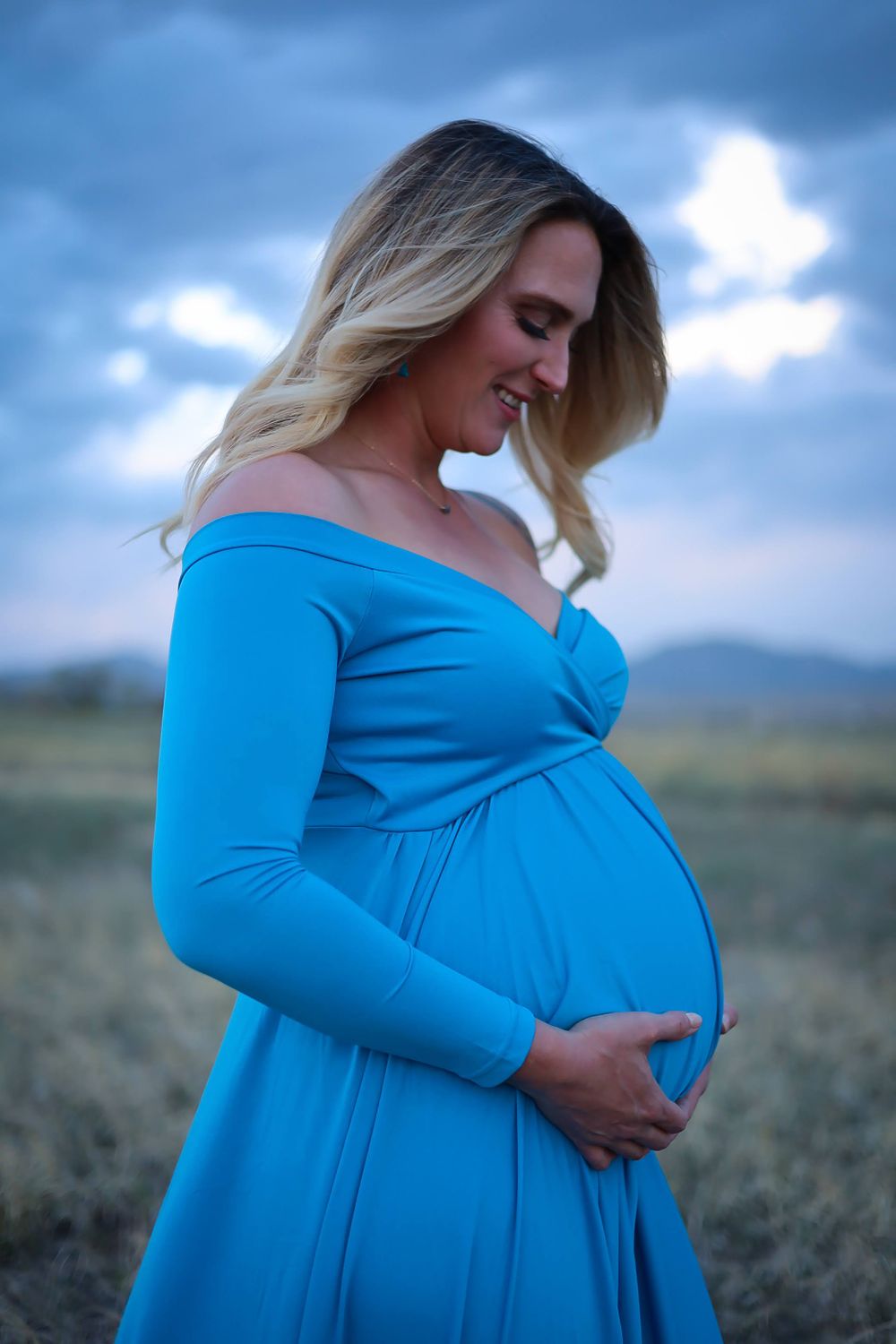Maternity portrait in bright blue dress against dramatic sky.