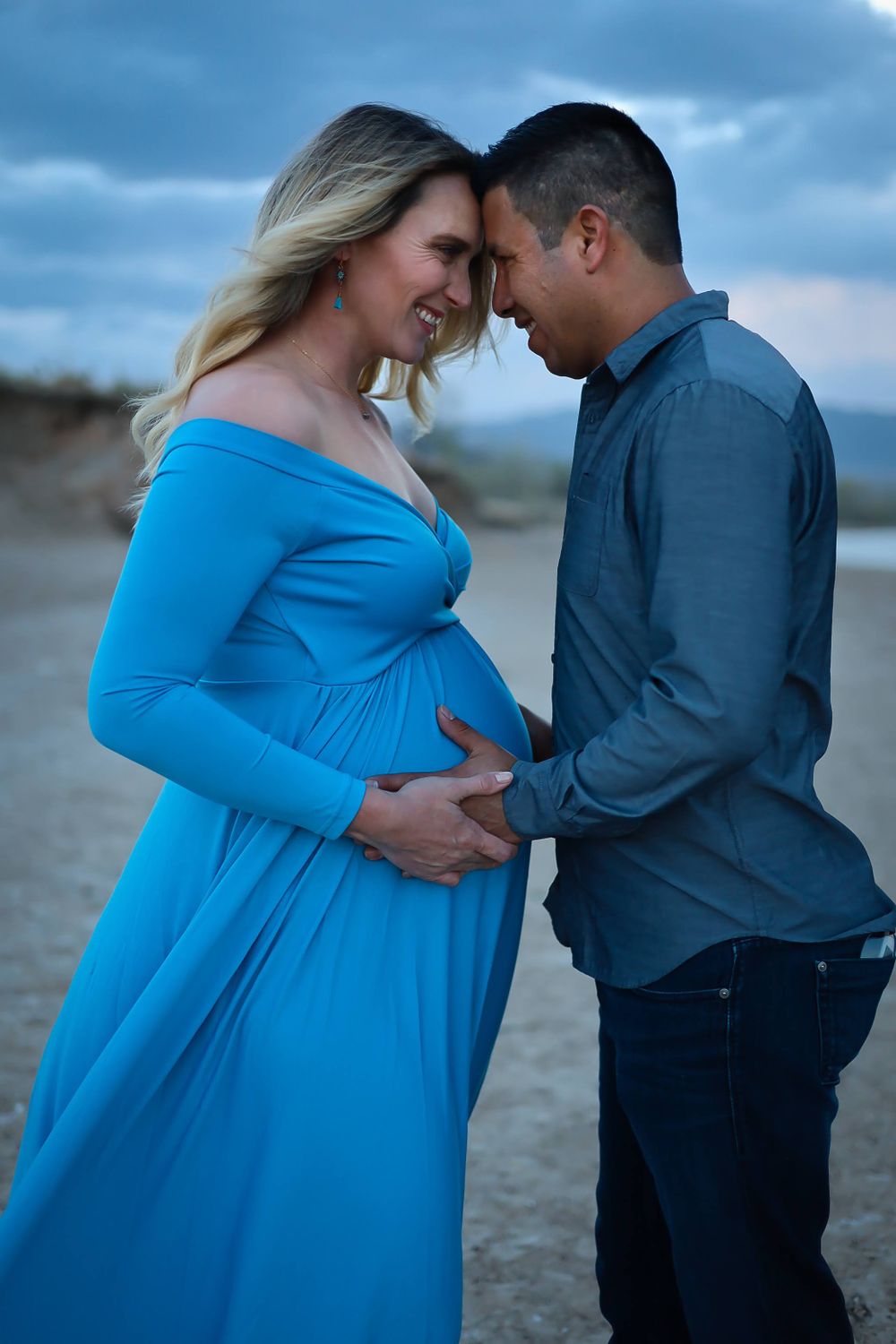 Intimate maternity portrait at sunset with couple in blue dress and navy shirt.