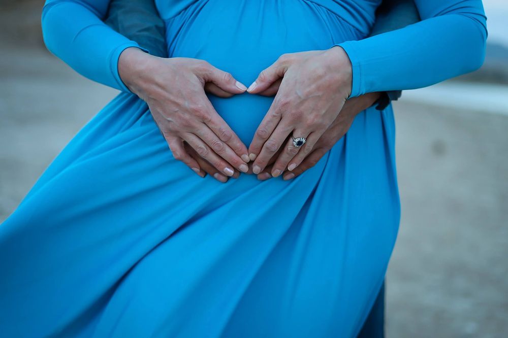 Close-up of hands forming heart shape on blue maternity dress.