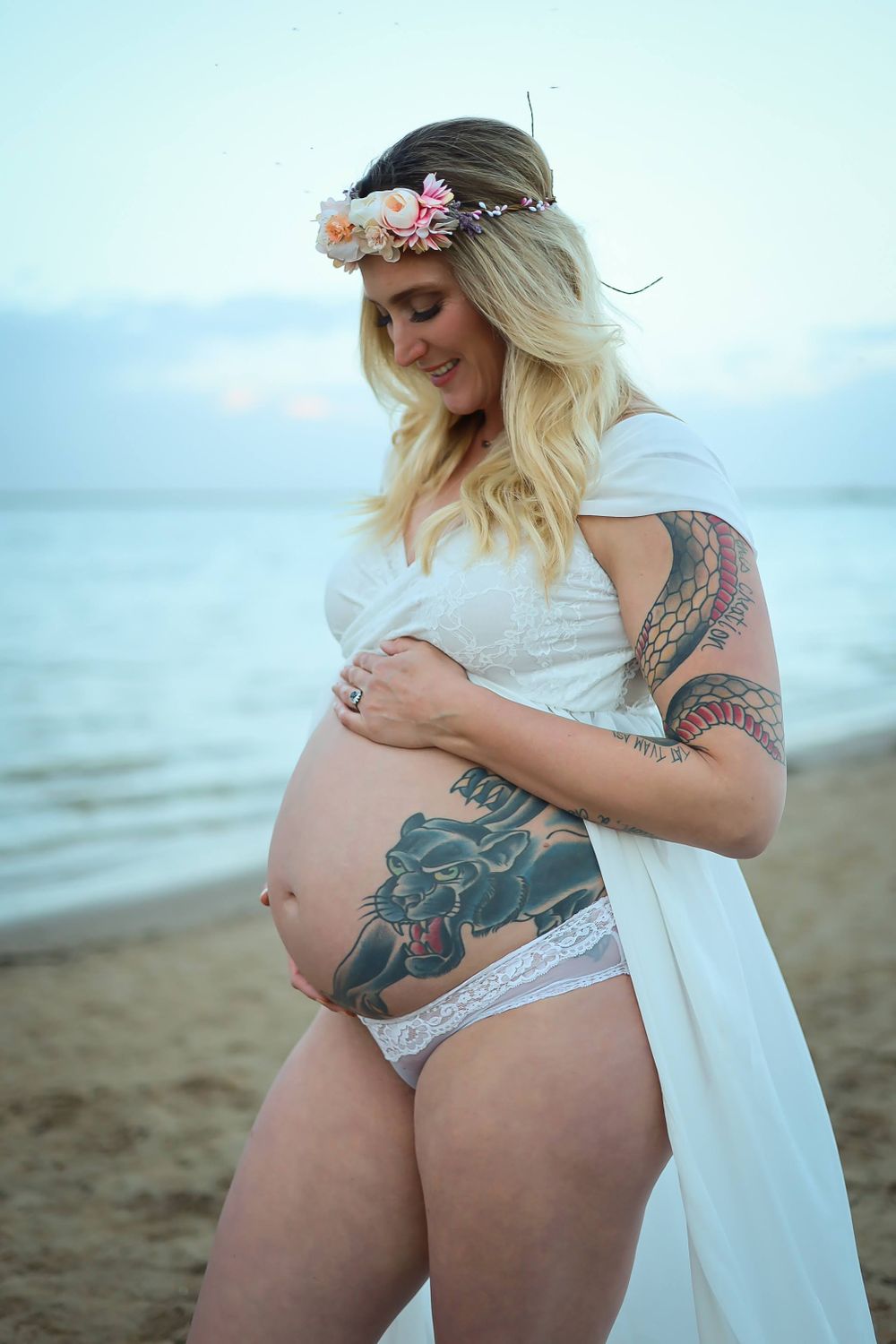 A maternity photo shoot on the beach featuring a flowing white dress and floral crown.