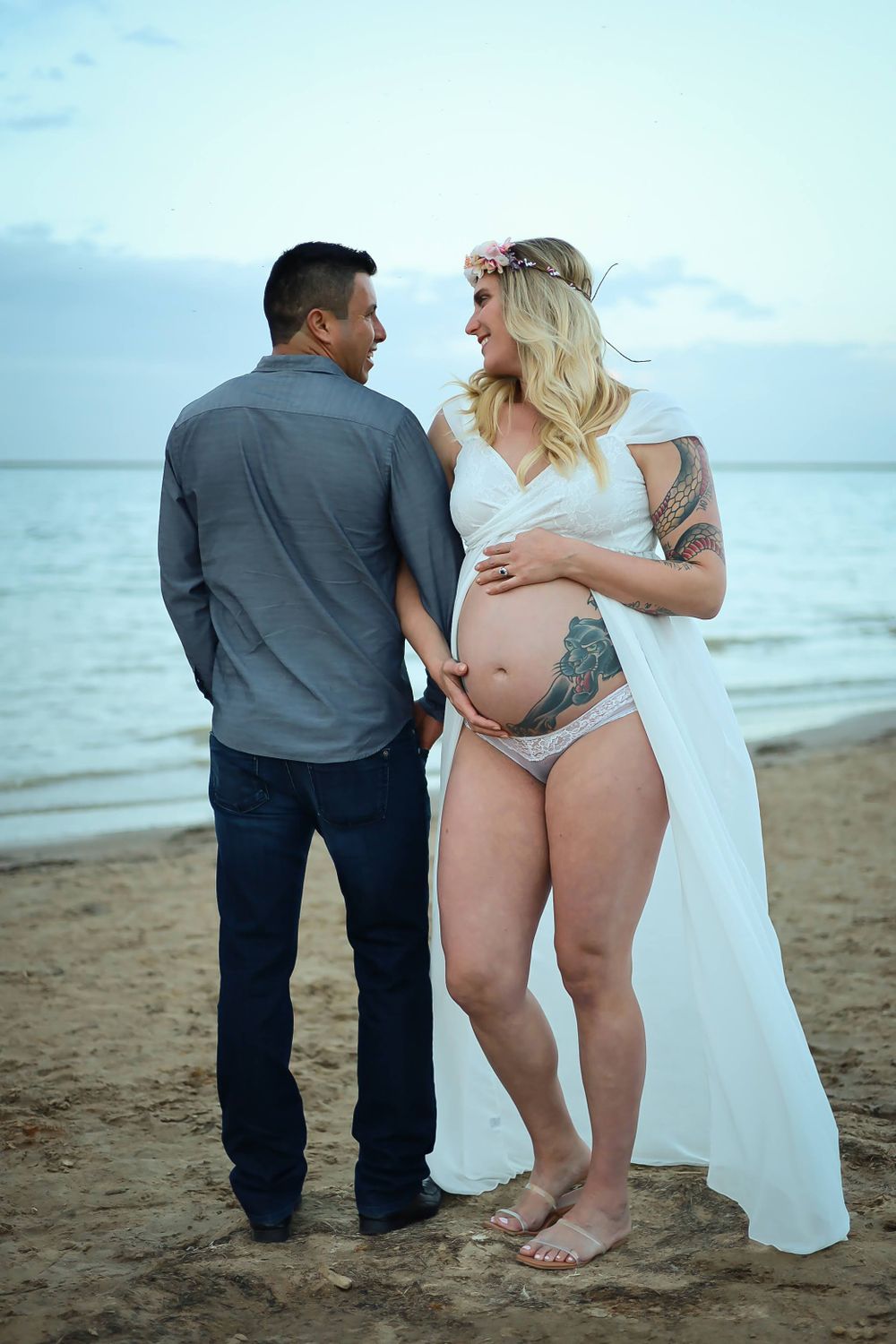 An intimate maternity photo shoot of a couple embracing on a beach at dusk.