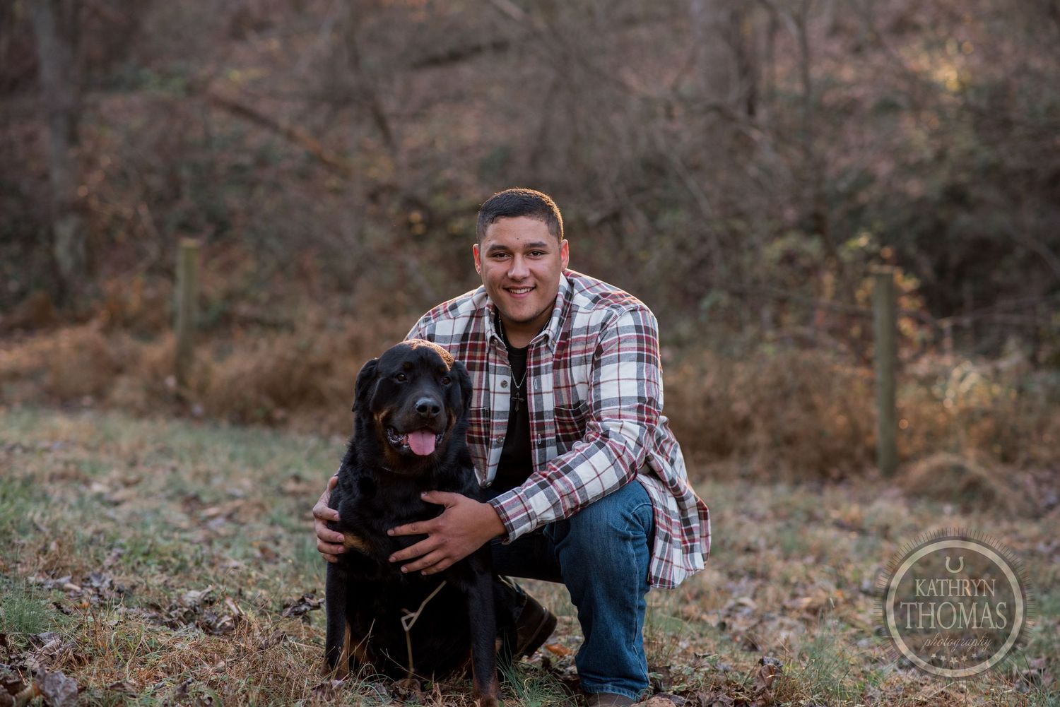 Person kneeling beside black dog for portrait in autumn forest setting.