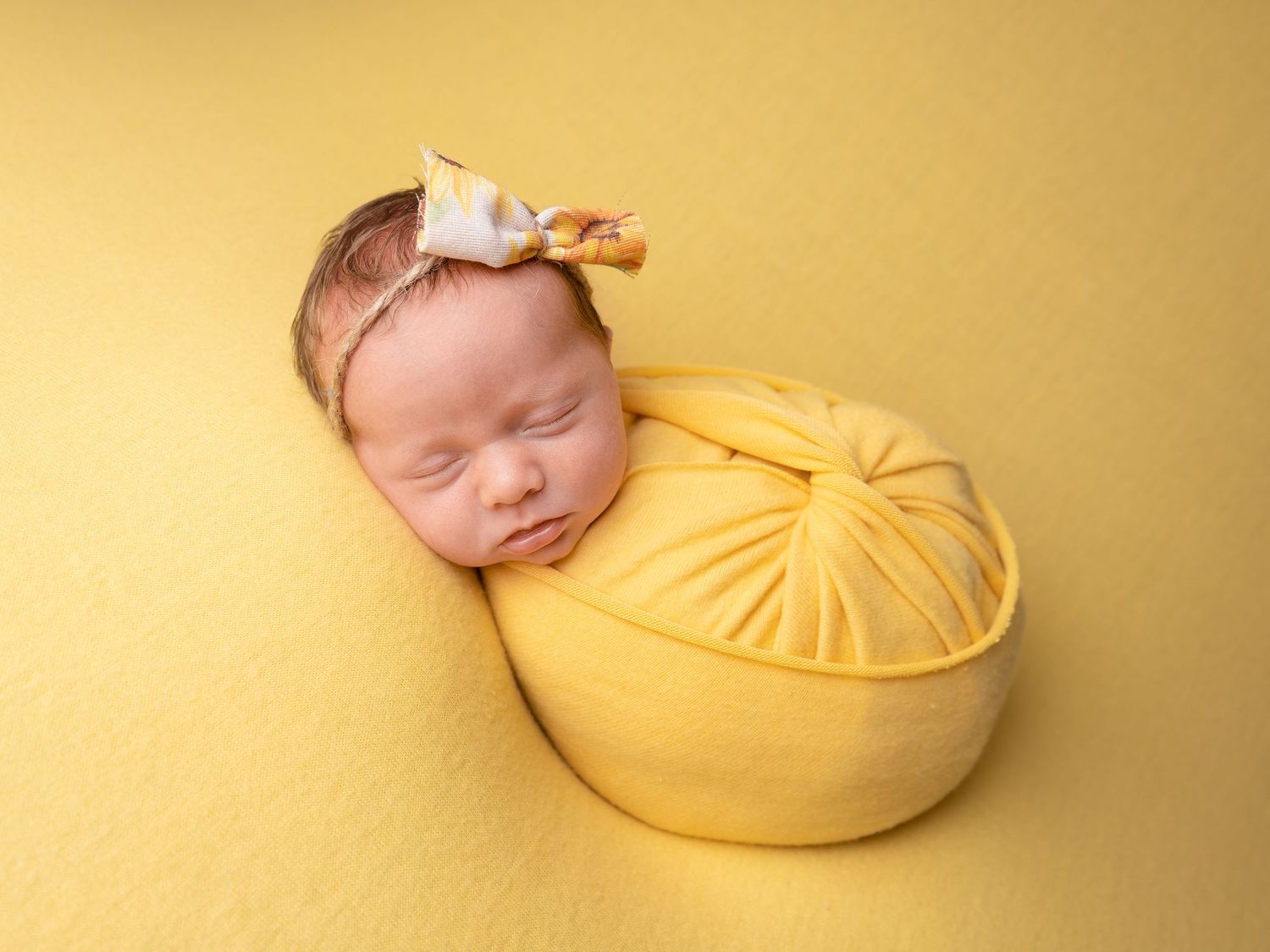 Baby girl sleeping wrapped in yellow wearing a sunflower headband at newborn photoshoot in Doncaster.