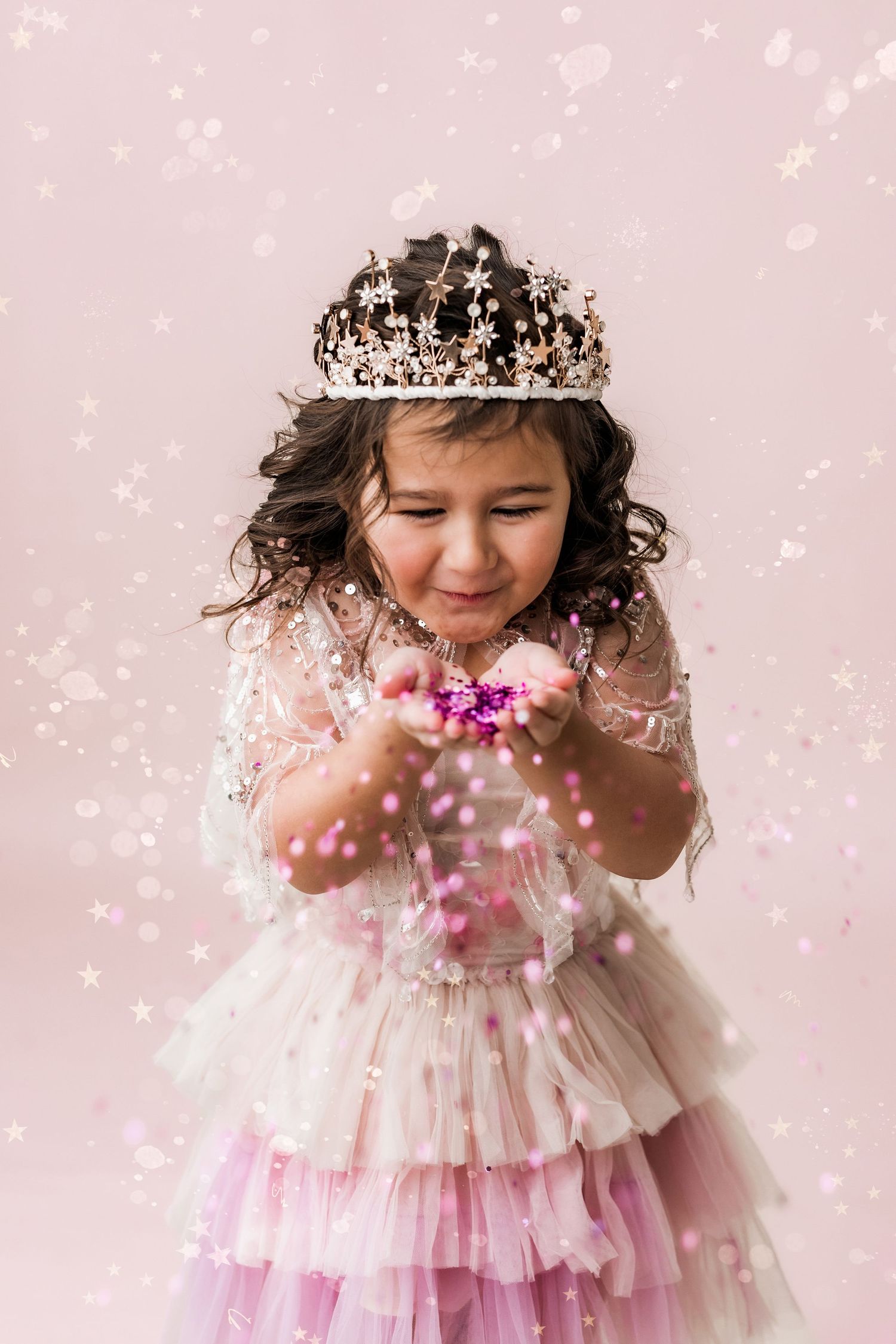 little girl in tiara blowing pink glitter