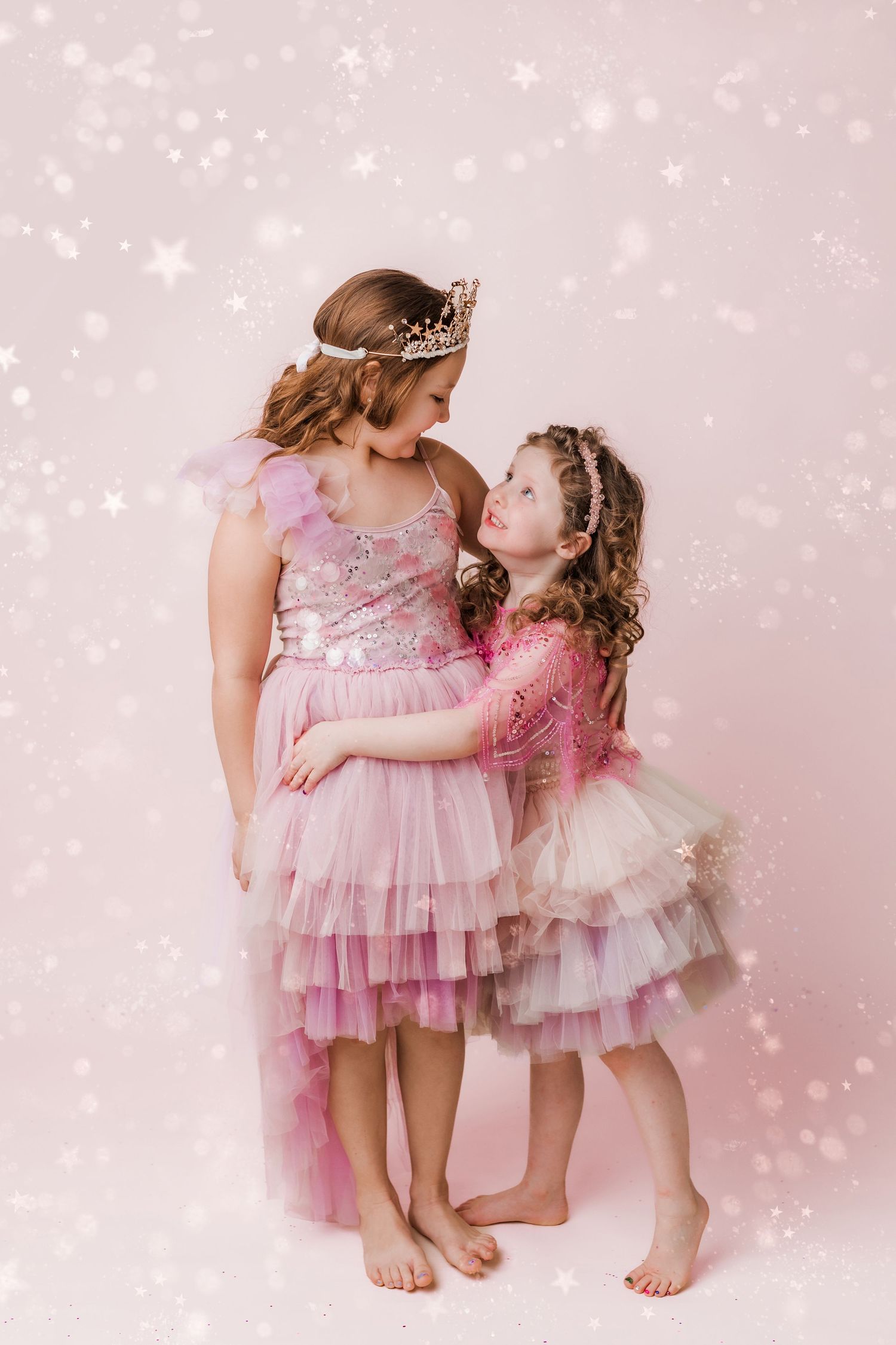 two girls dressed in princess dresses and tiaras hugging